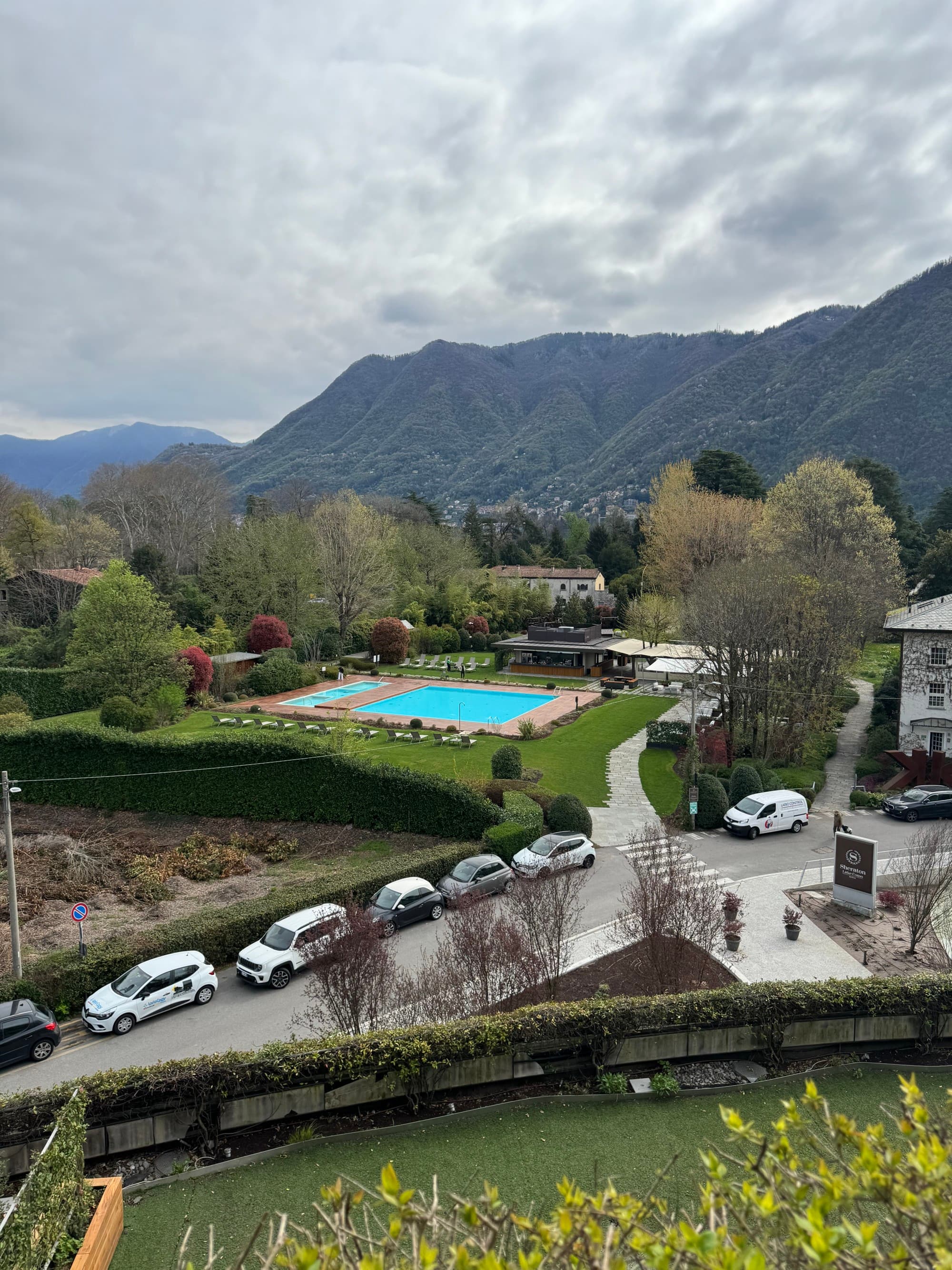 A view of a mountain valley neighborhood with other houses, cars and a backyard pool on an overcast day.