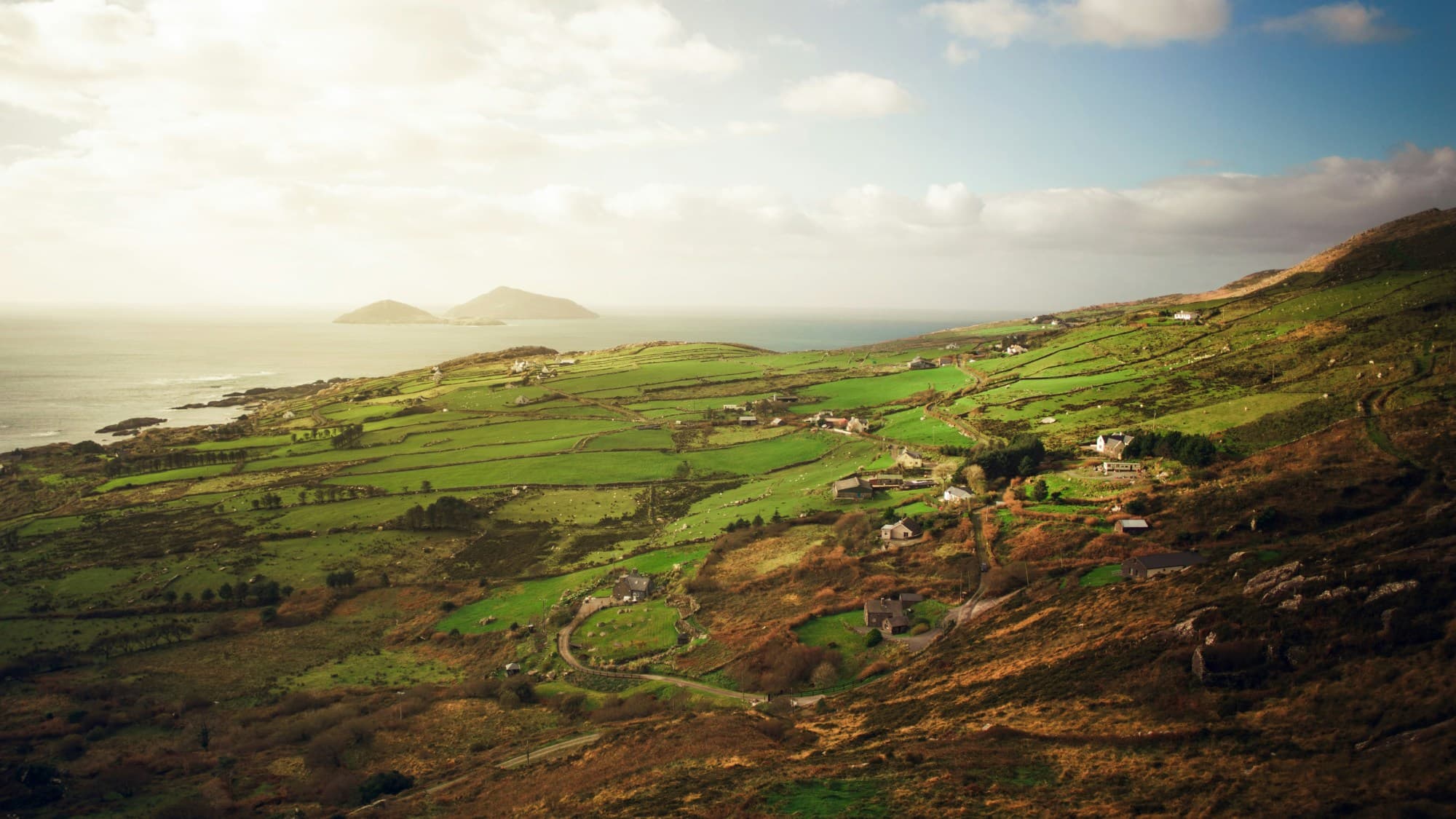 An aerial view of the green Irish landscape and sea on a golden-sunny day in November.