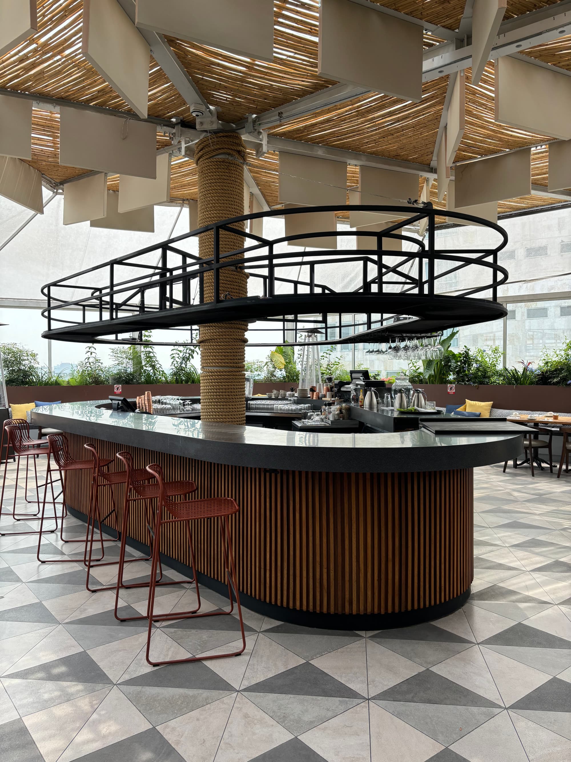 A brown and black, modern, oval-shaped bar set in the middle of a spacious and bright restaurant.