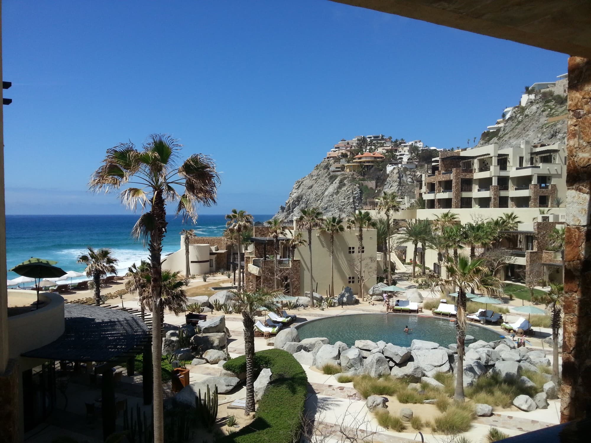 A view of the sea behind beige buildings and a pool area