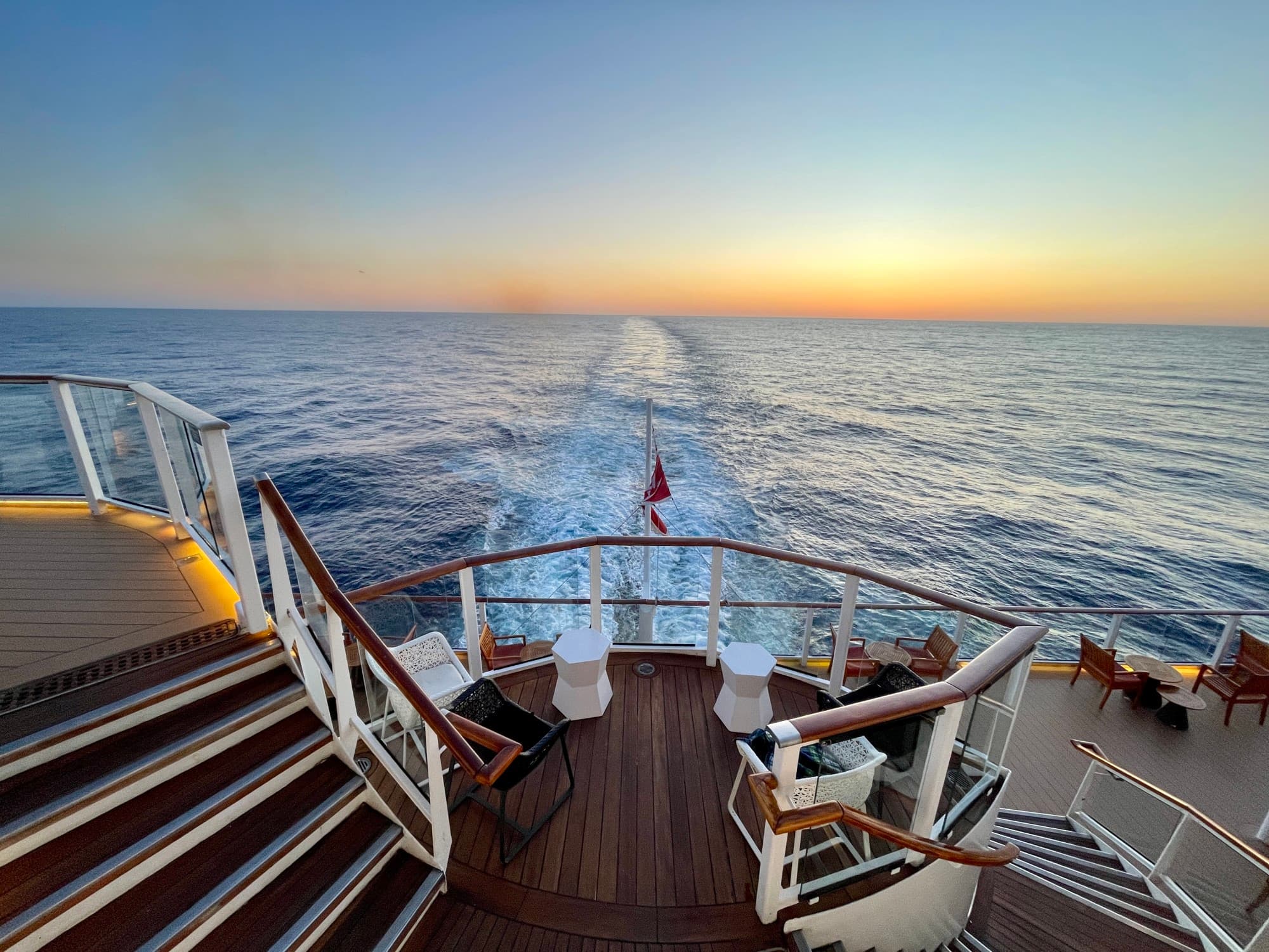 A view of the stern of a Celebrity cruise ship, and the sun setting over the water.