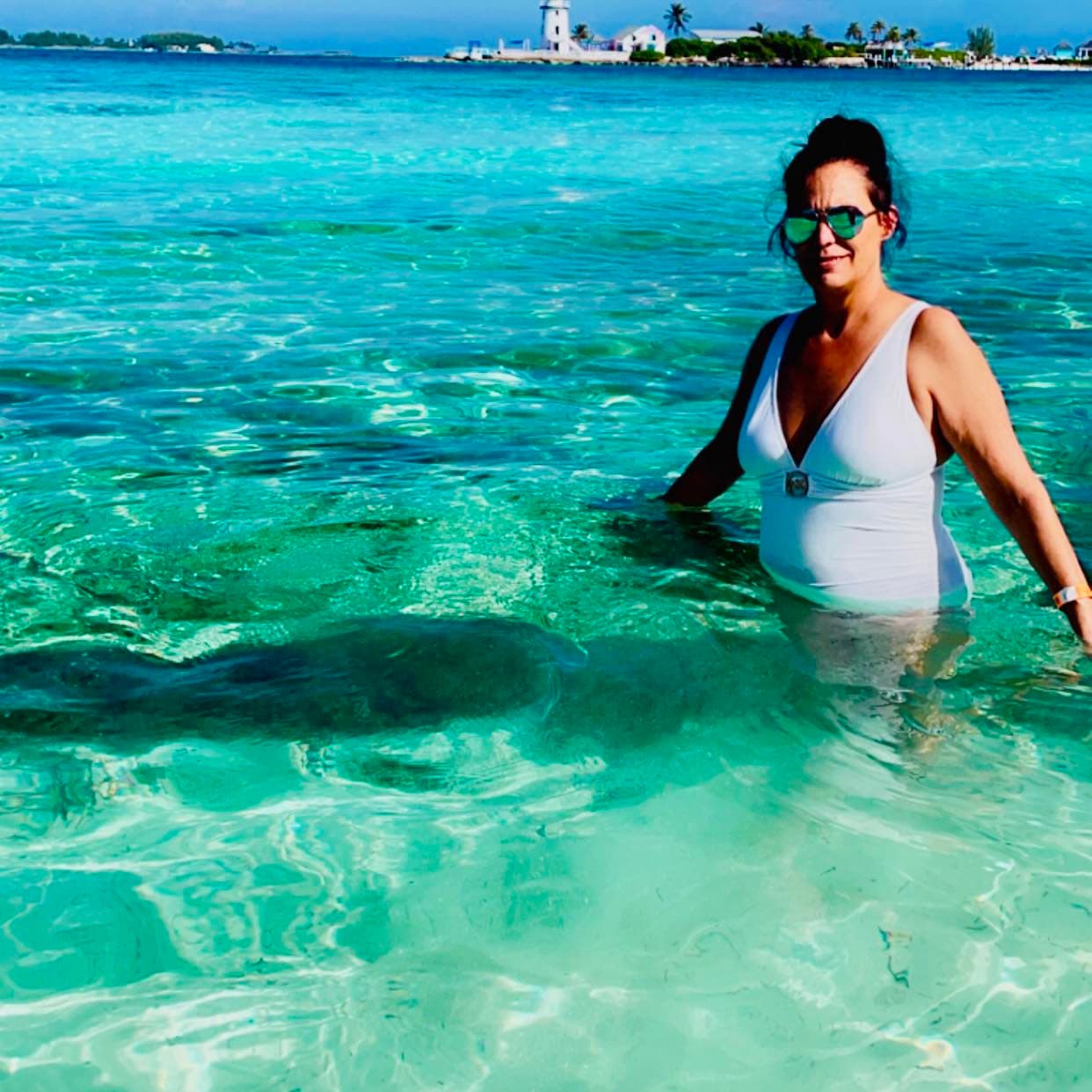 Jennifer waist-deep in the clear, turquoise waters of the Bahamas, with the coastline in the background.