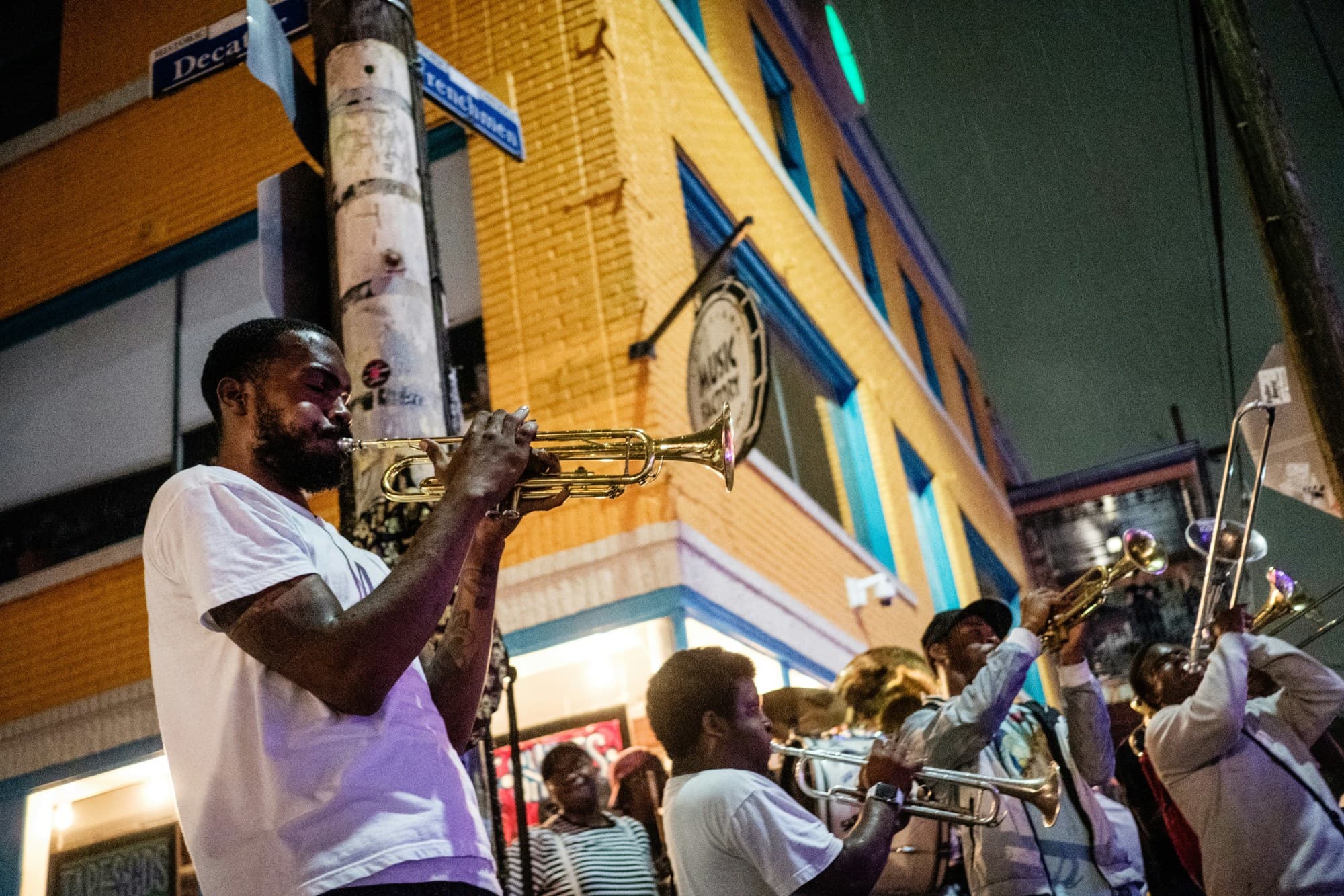 A group of people playing brass instruments in a crowd outdoors on Royal Street, New Orleans with a yellow colored building behind