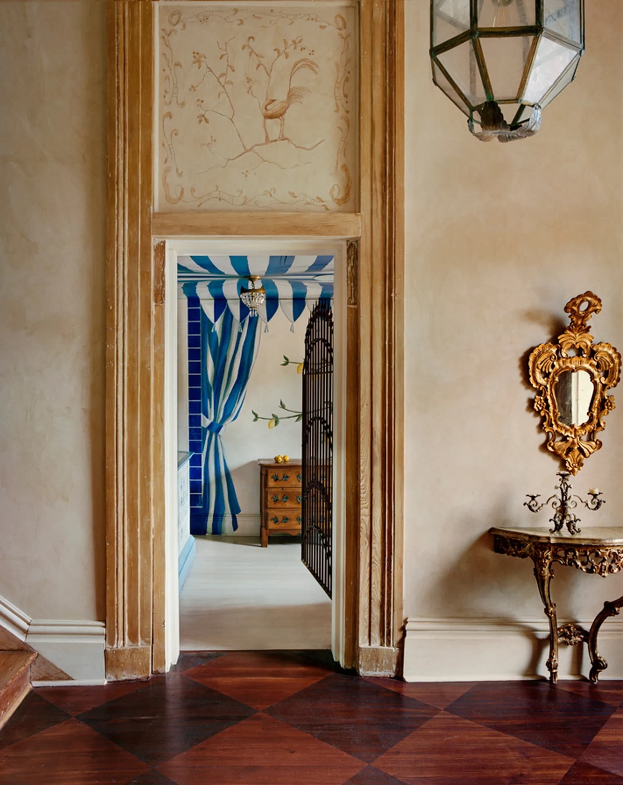 A grand foyer with a hard-wood floor and decorative table and mirror, with an open door leading to a hotel room at the Hotel Peter and Paul, New Orleans.