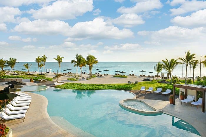 A turquoise pool overlooking a beach with umbrellas and the ocean