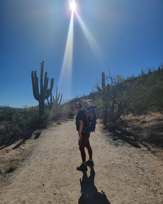 Picture of Ashlyn hiking on a dirt road with large cacti on a sunny day