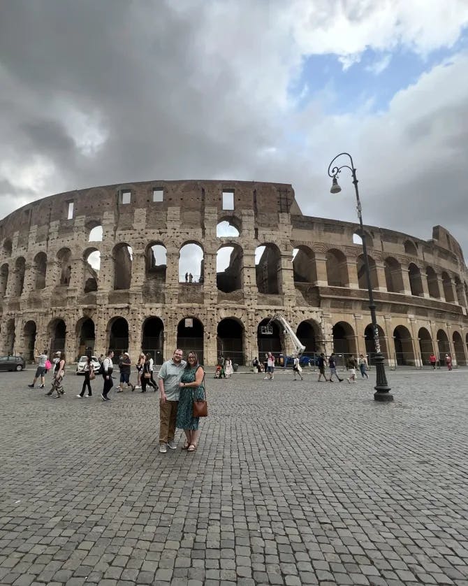 Couple posing in front of the Colosseum in a large open pedestrain area with many people in Rome