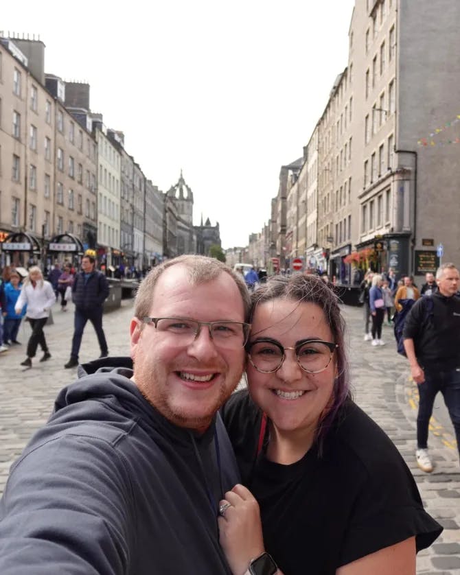 A couple posing for a selfie on a busy street with many people walking