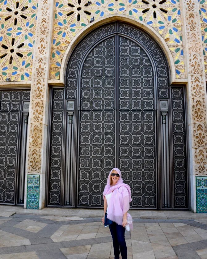 Travel advisor Allison wearing a purple shawl over her head and neck standing in front of a large arch-shaped doorway surrounded by ornate decoration