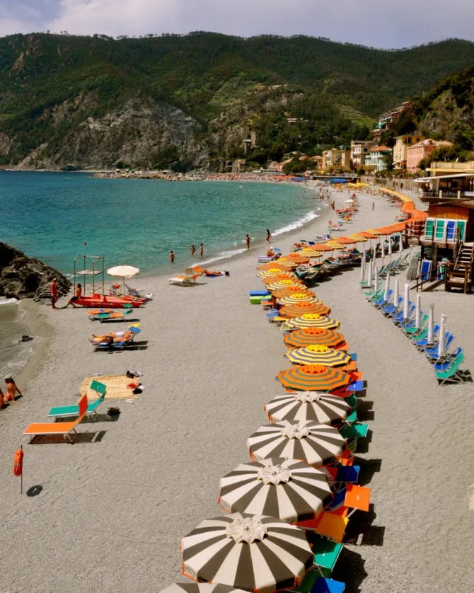 A beautiful beach with a long row of colorful umbrellas and hills in view