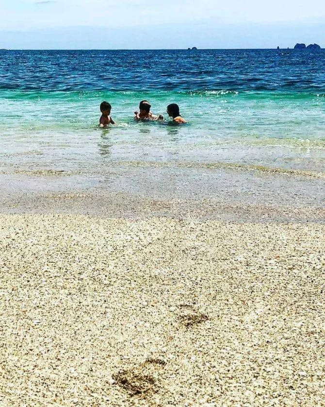 Picture of April with kids sitting in crystal clear water on a yellow sandy beach