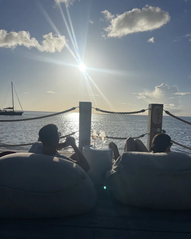 A man and a woman drinking wine and lounging on a deck with drinks overlooking the sea