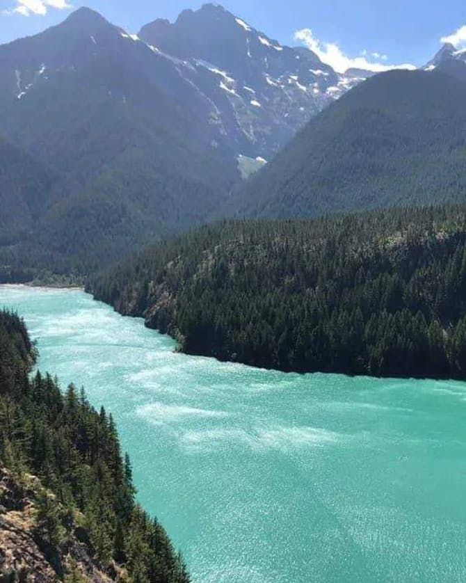 View of a clear blue lake, surrounded by mountains and forest on all sides, from above