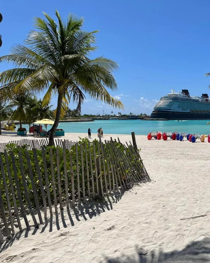 A view of a beach with turquoise colored water and palm treets, and a cruise ship in view