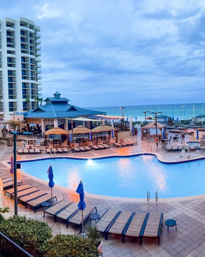 View of the outdoor pool with sun loungers and the beach in view at Hilton Sandestin Beach Golf Resort & Spa taken in the evening.