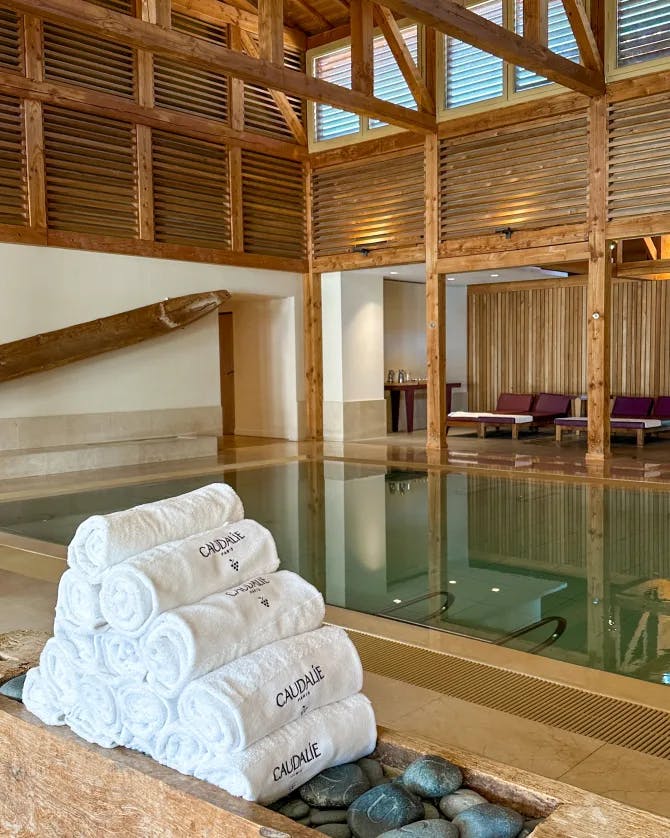 White towels rolled up near a swimming pool inside of a wooden building with ceiling beams