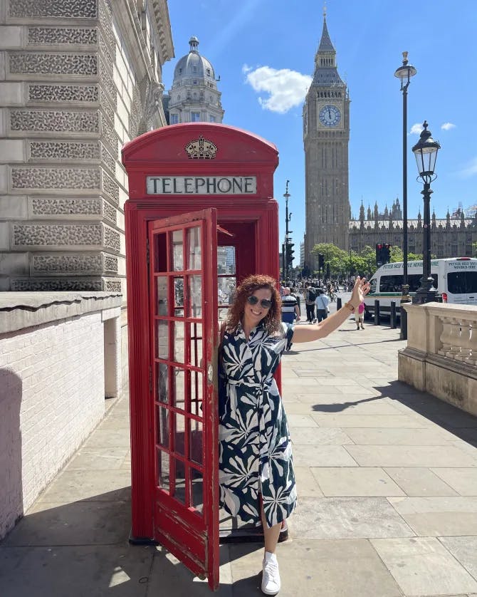 Travel advisor Alexandra coming out of a red phone booth in London with Big Ben in view on a sunny day