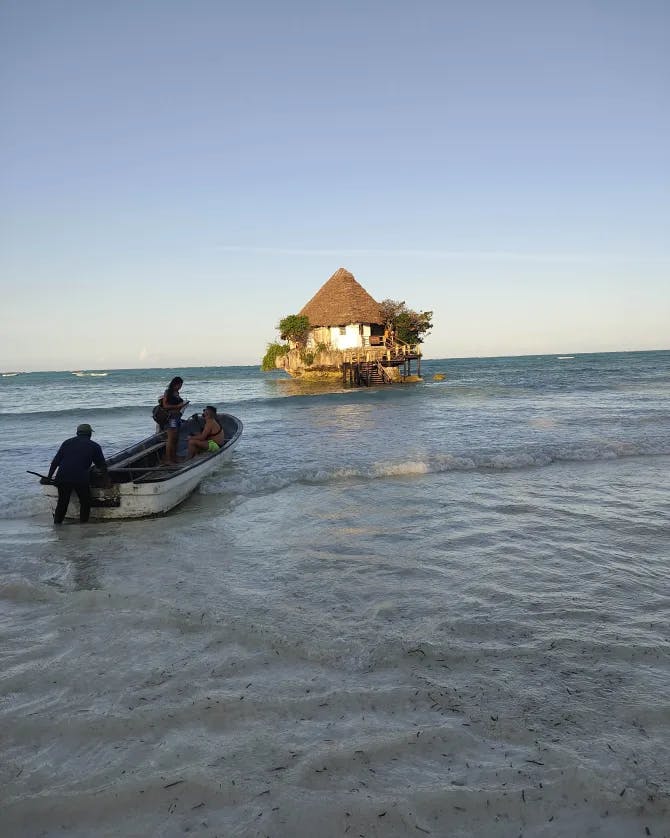 Two people on a rowboat in the water near an overwater hut.