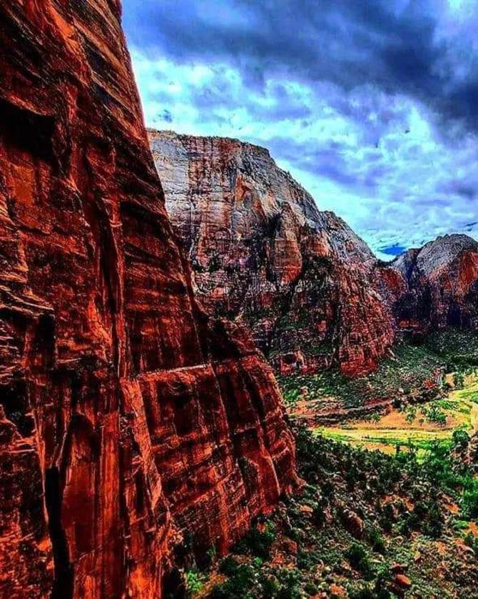 View of red, rock mountains with a bright green, lush valley below in Zion