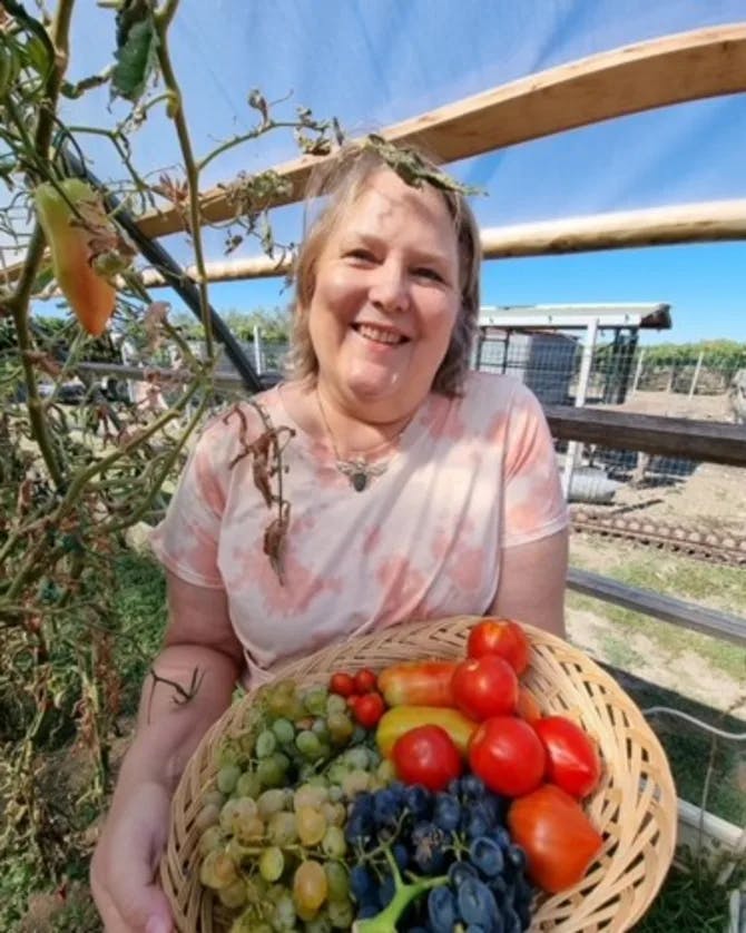 Bettina holding a basket of fruits in a garden.