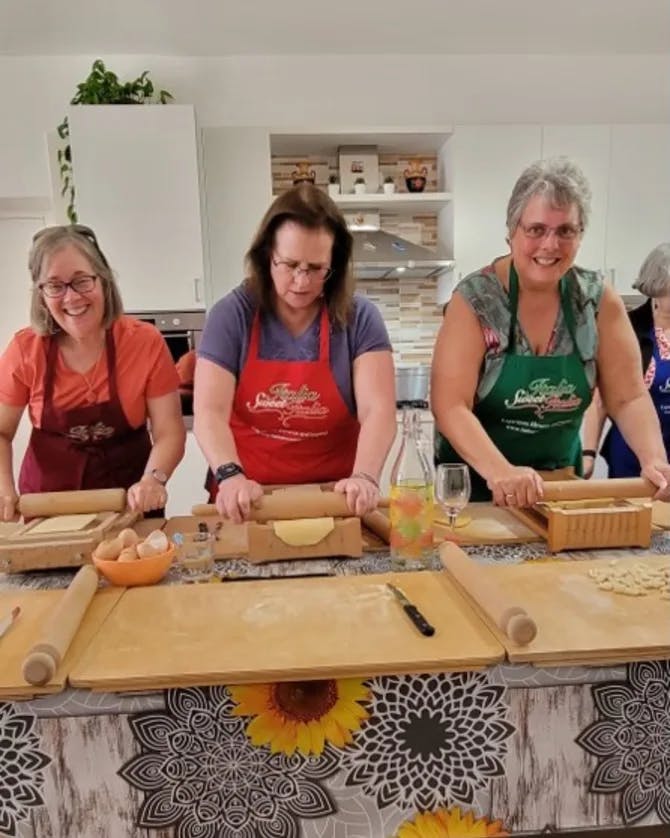 A cooking class with three women rolling out dough on a counter in a kitchen.