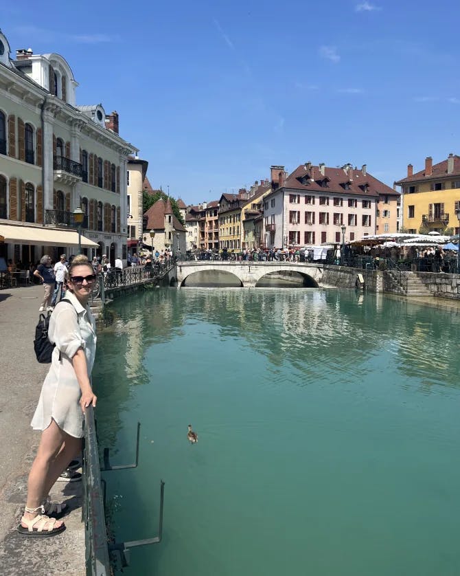 Keller posing for a photo at the Lake Annecy with a bridge crossing the lake in the view at a distance