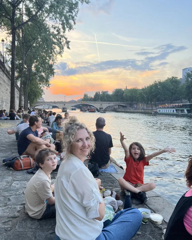 Keller sitting with children by the river and having a picnic at sunset