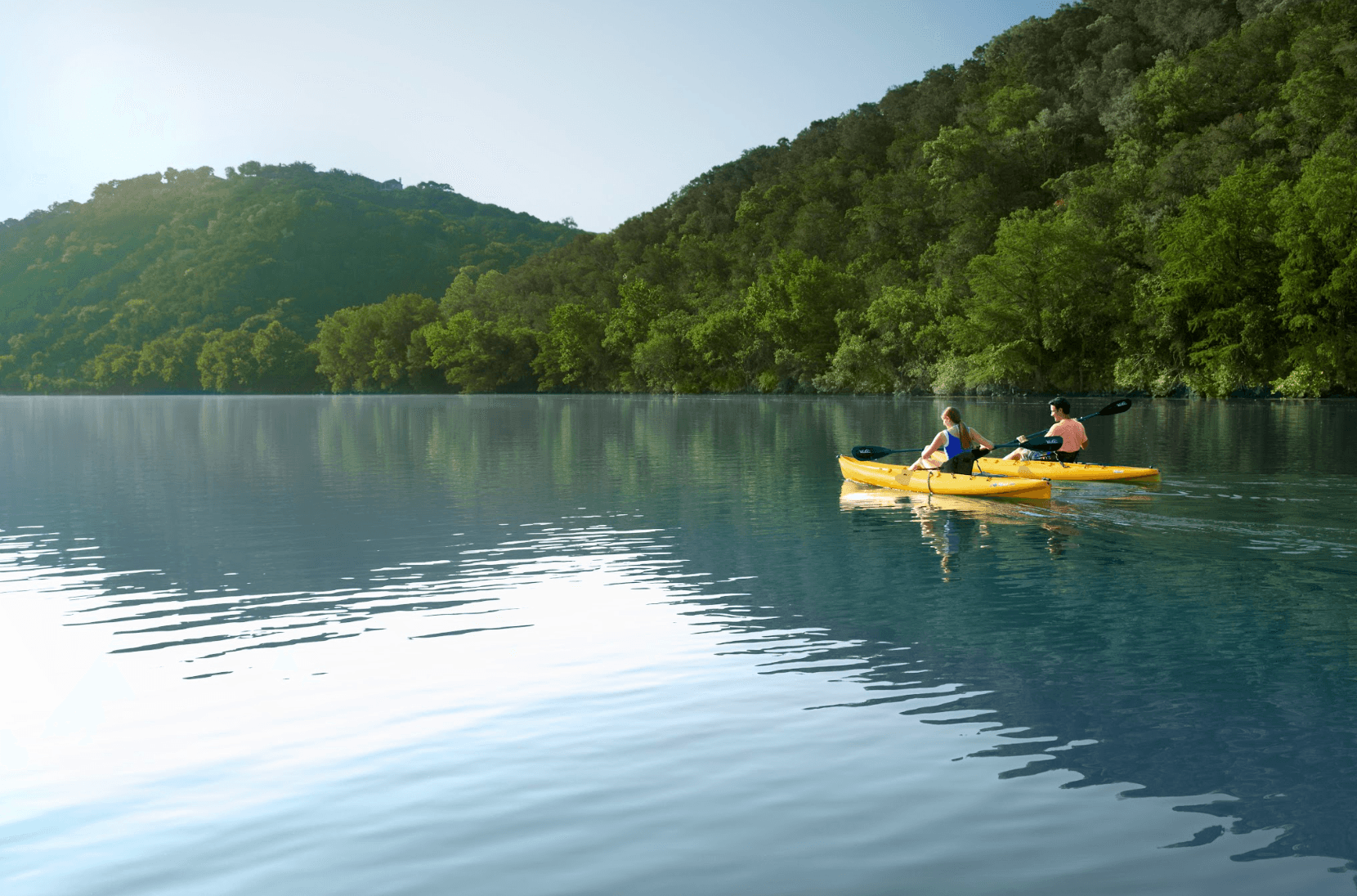 two people paddle yellow kayaks on a hillside lake