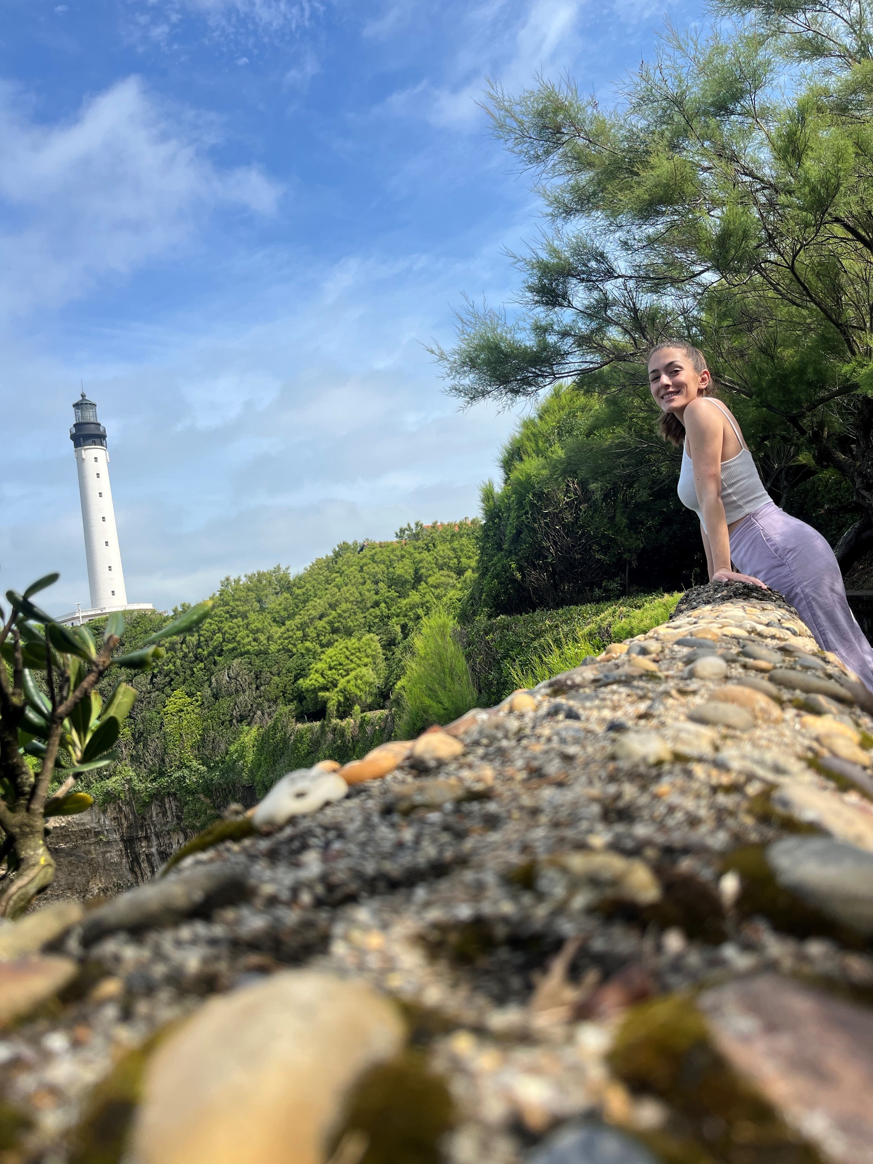 Stephanie posing against a rocky ledge with trees and a white lighthouse in the background.