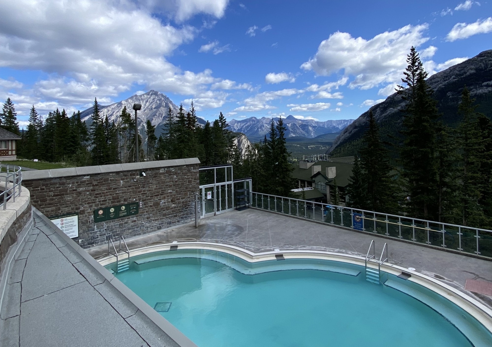 A pool in a resort surrounded by mountains and trees.