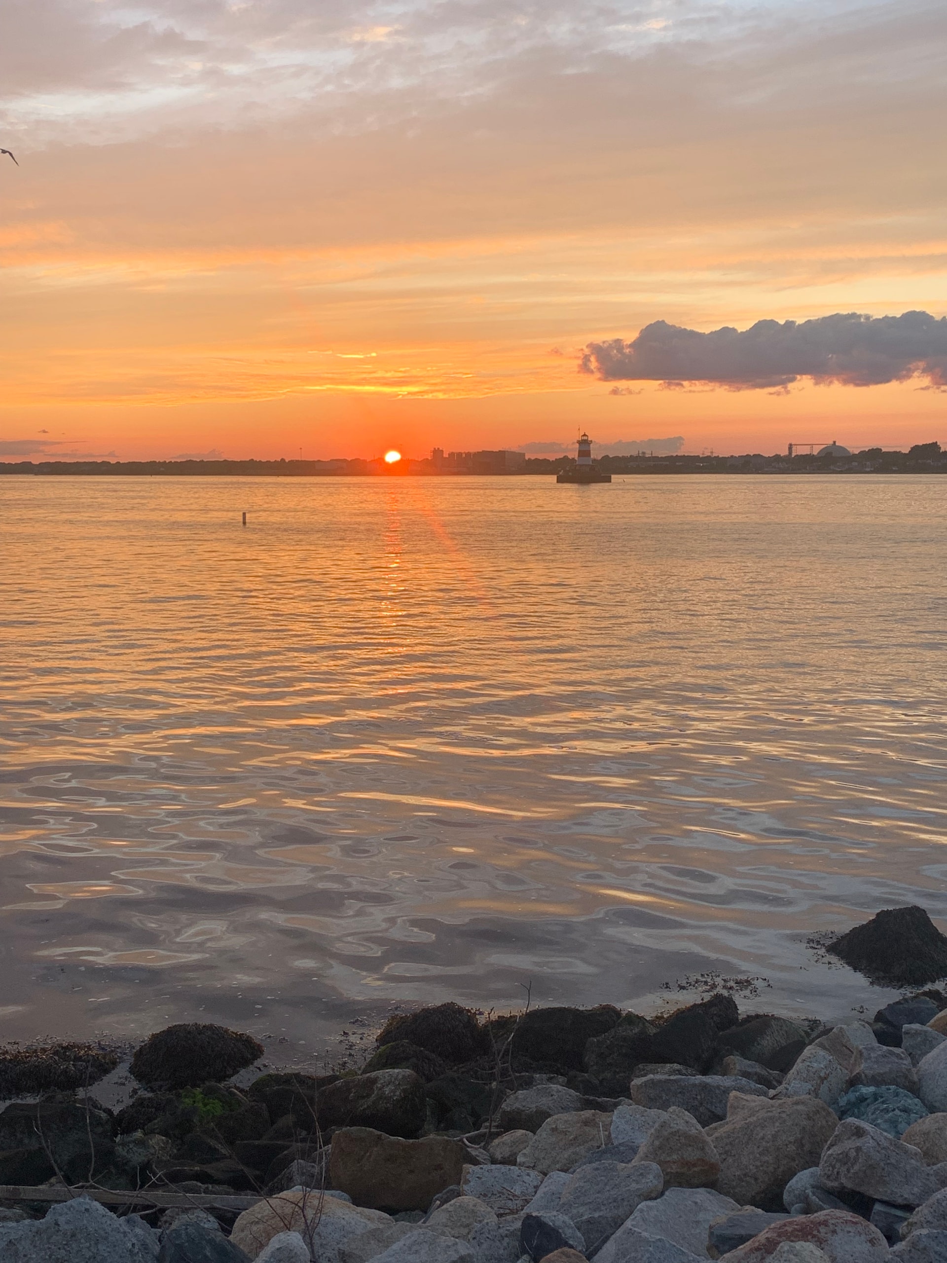 Golden sunset view over the harbor, with beach rocks in the forefront.