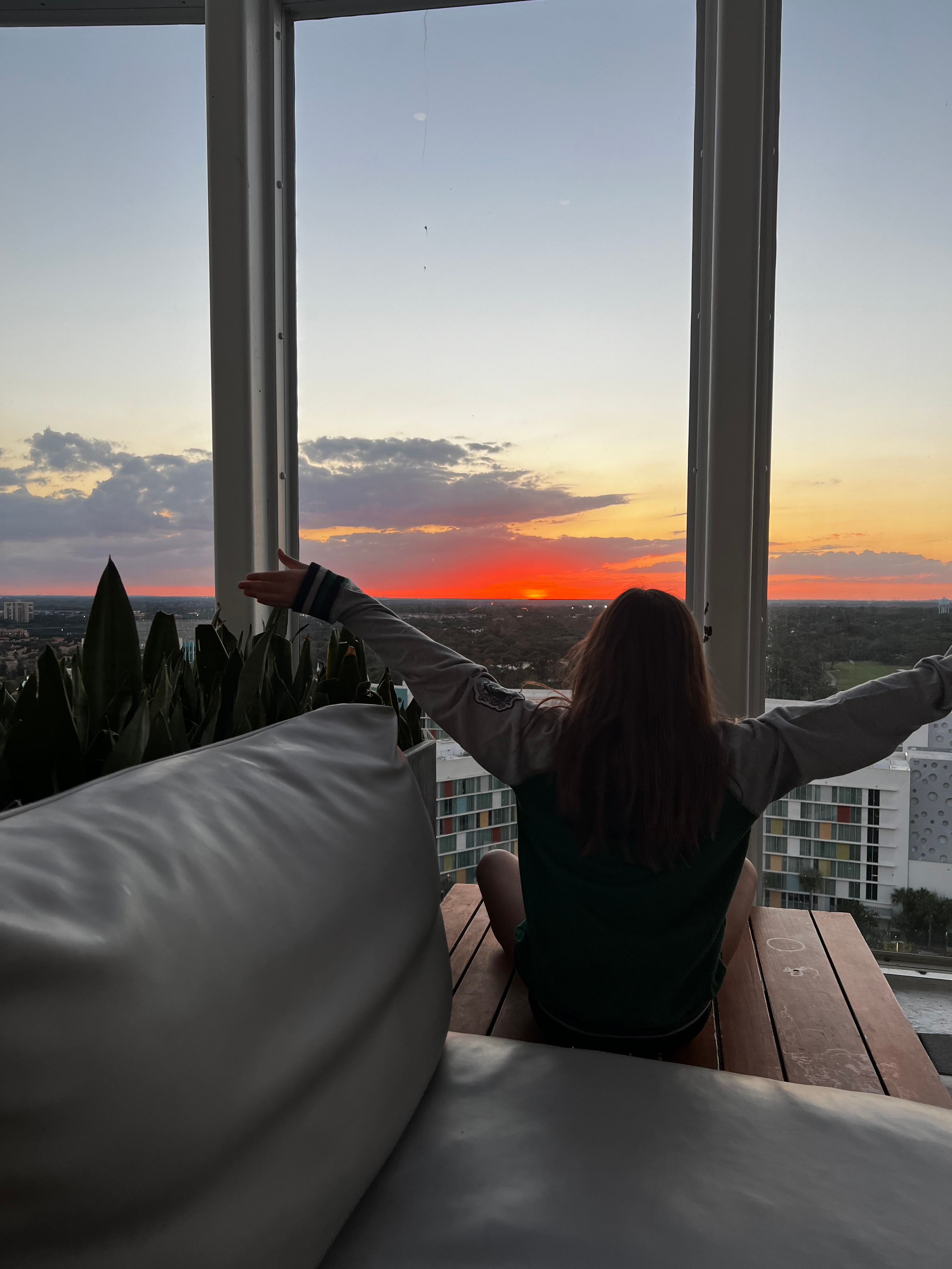 Picture of Amanda watching sunrise from a bedroom while sitting on a wooden floor with her arms spread open 