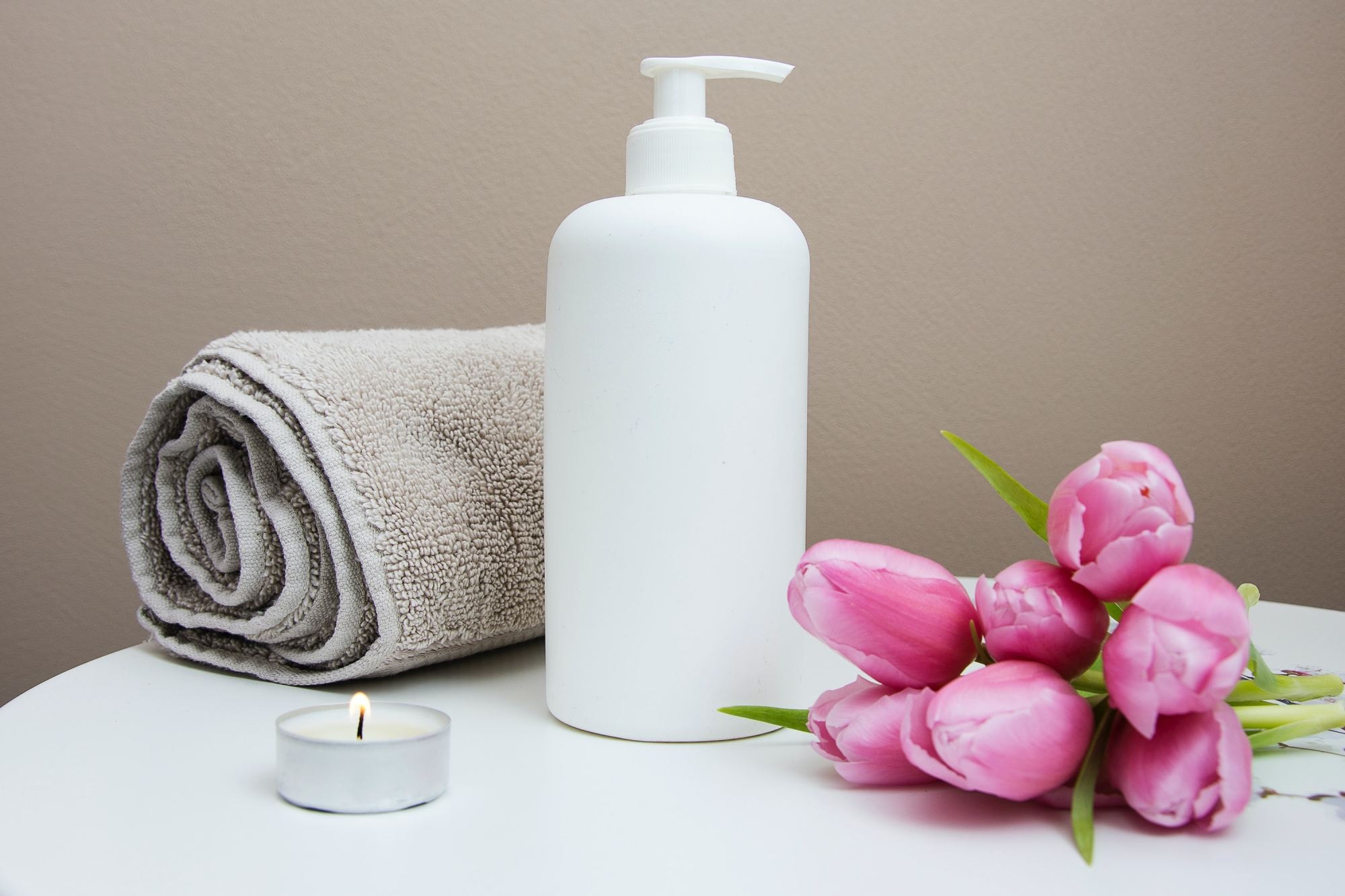 White plastic pump bottle beside pink tulips and gray towel.