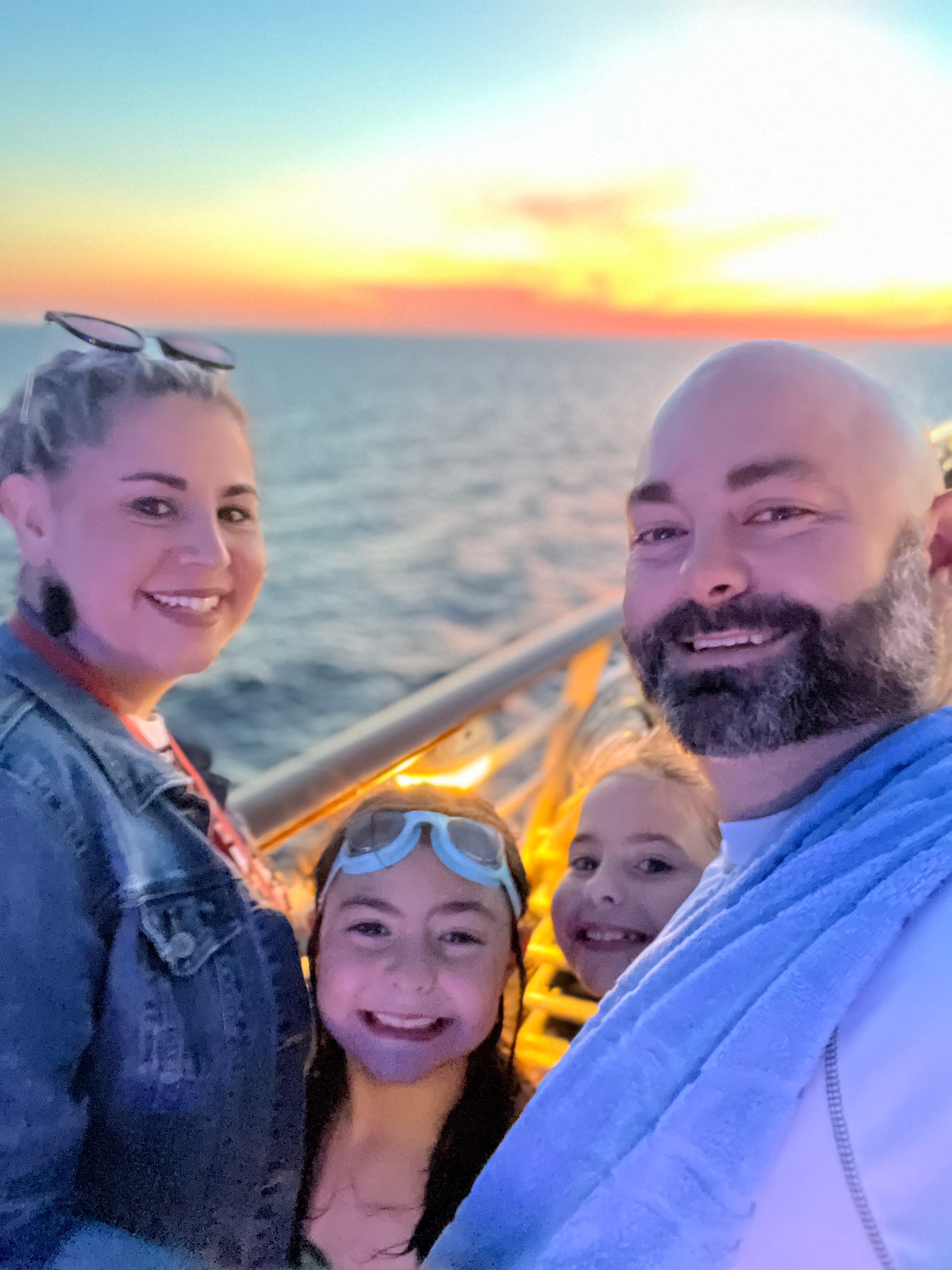 Picture of Amanda with a man and two children on the beach in front of a sunset and bonfire 