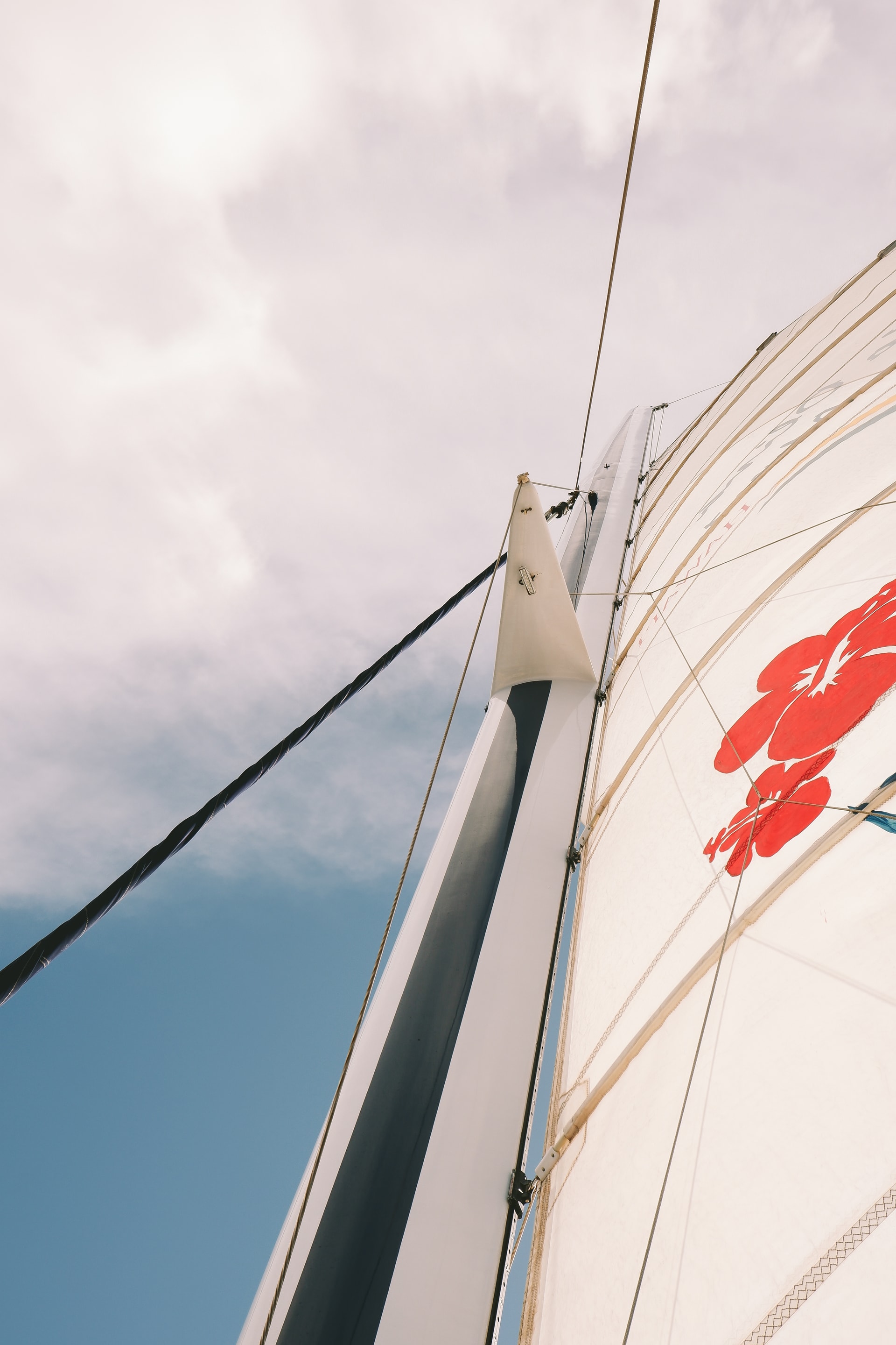 View of a sail on a sail boat with a red design and a cloudy blue sky in the background