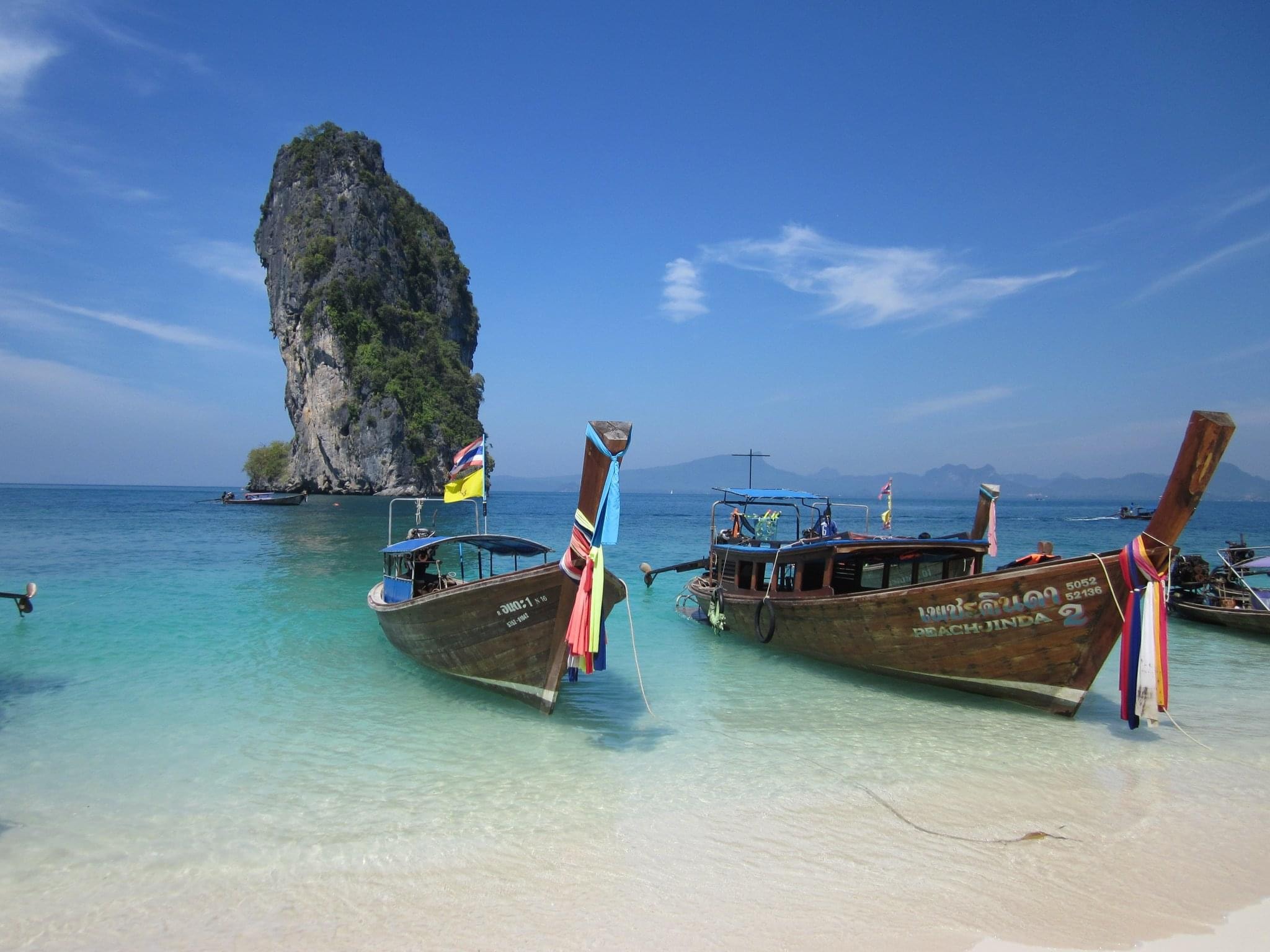 Two wooden boats anchored on a shoreline over turquoise blue water with a rock formation in the background