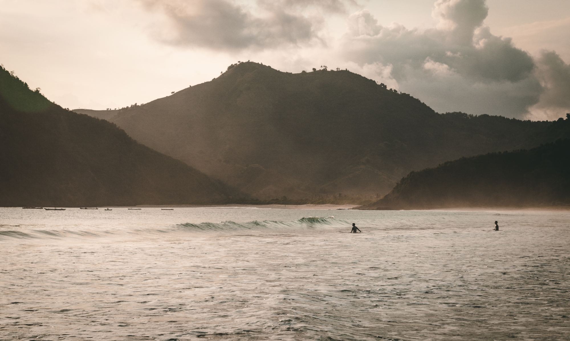 A couple of people surfing in the sea with mountains in the background. 