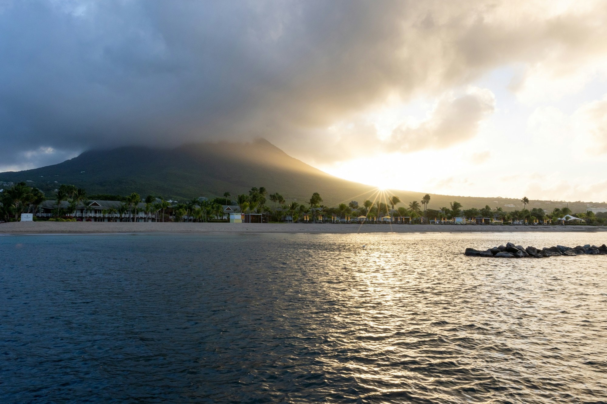 A large body of water with a mountain in the background during sunrise.