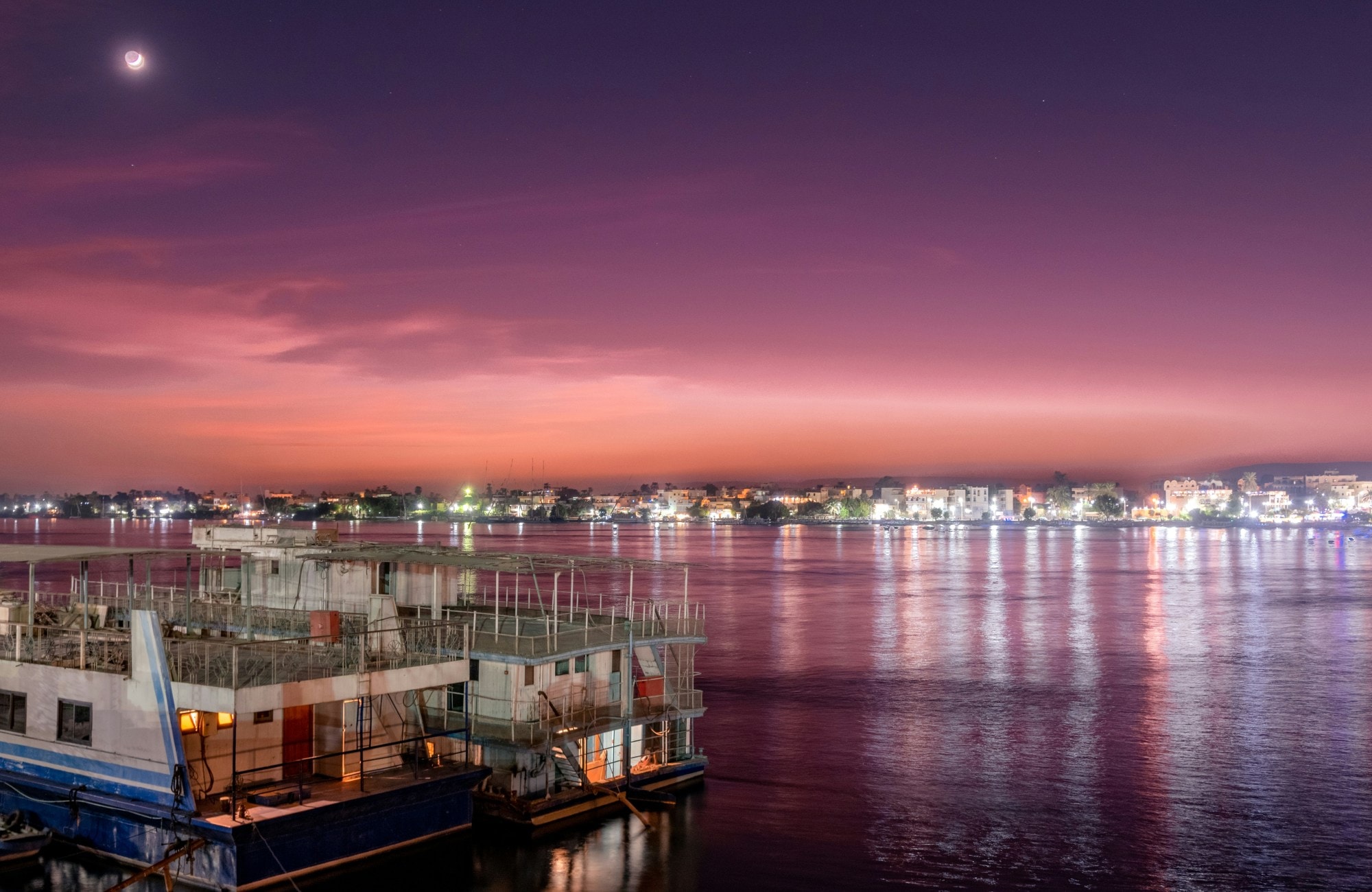 A river with city lights and a big boat at its bank. 