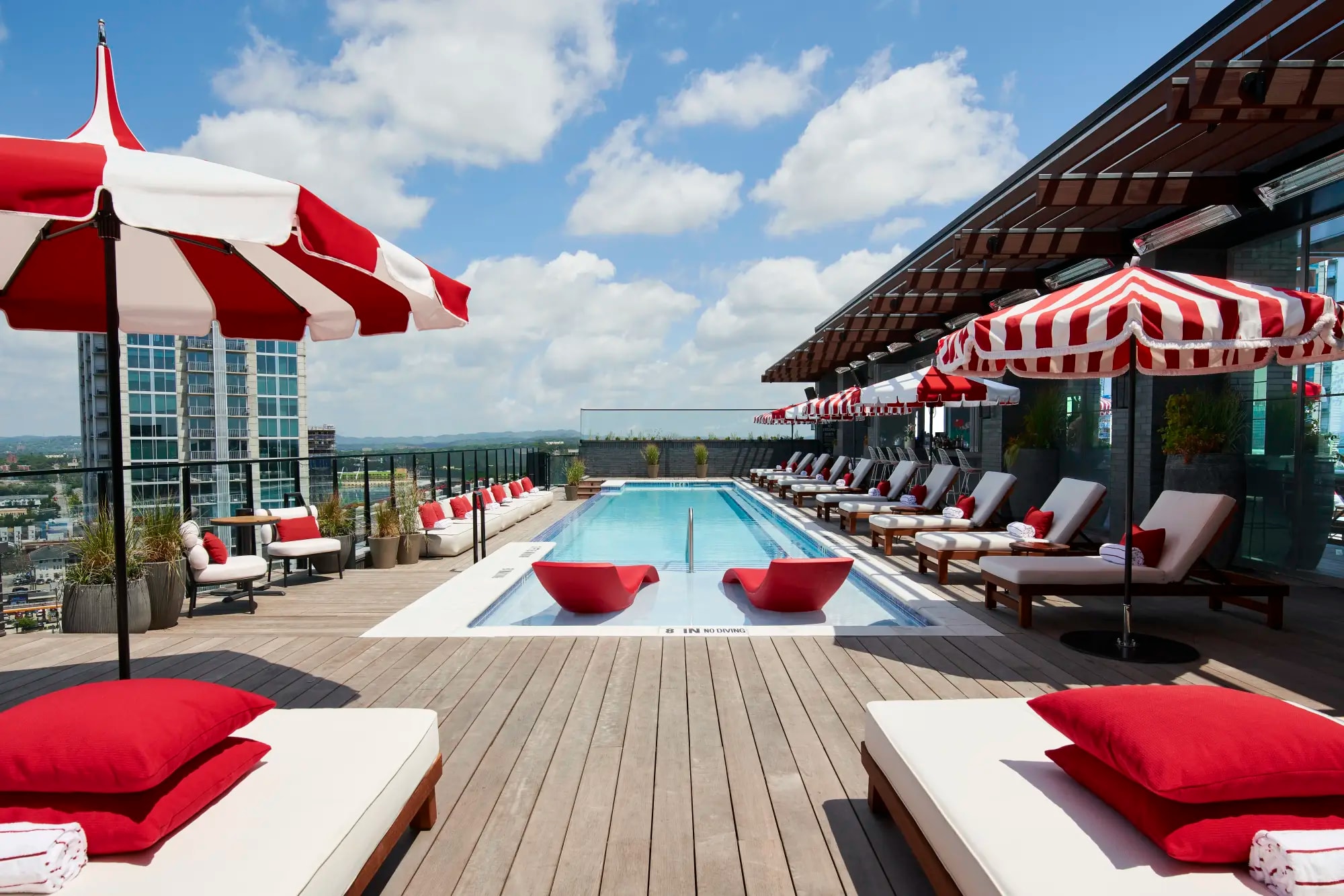 a rooftop pool surrounded by red lounge chairs and red-and-white striped umbrellas