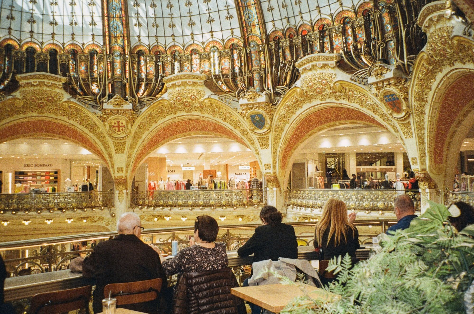 A group of people sitting at tables in a restaurant inside a mall with golden fancy interior. 