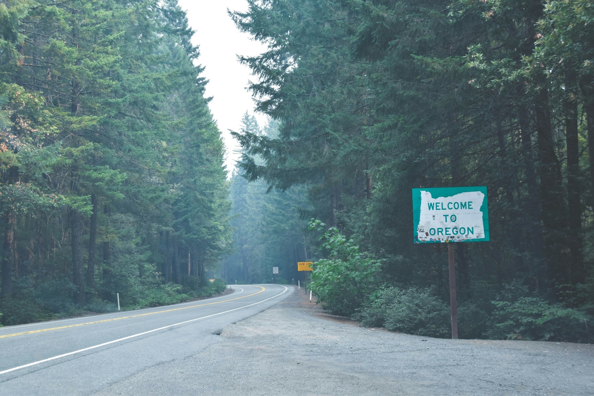 A road between trees with board saying Welcome to Oregon.