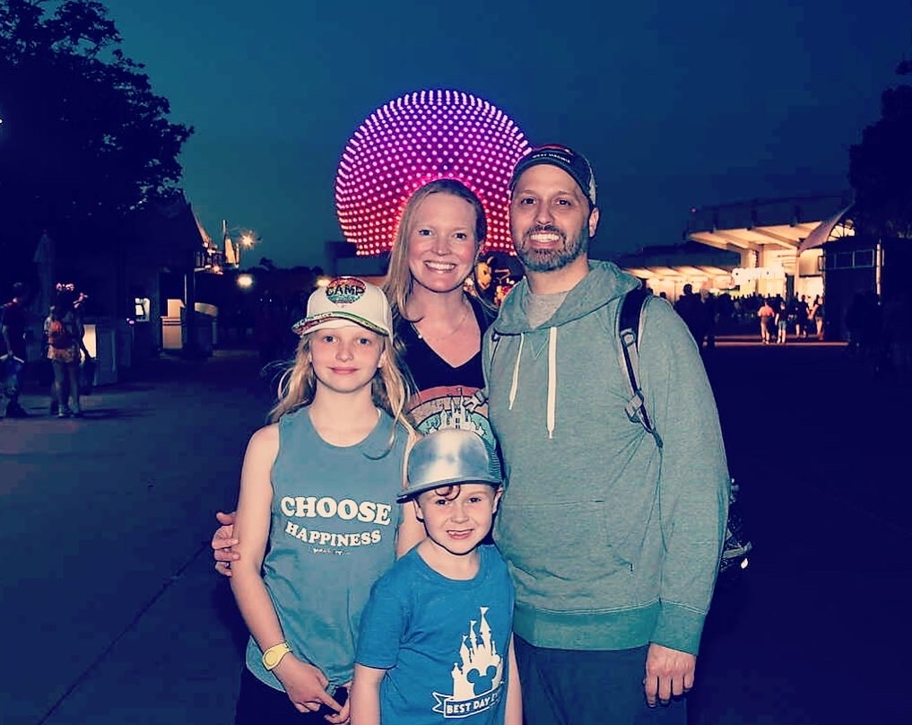 A family posing for a photo at an amusement park with a round pink light feature in the background