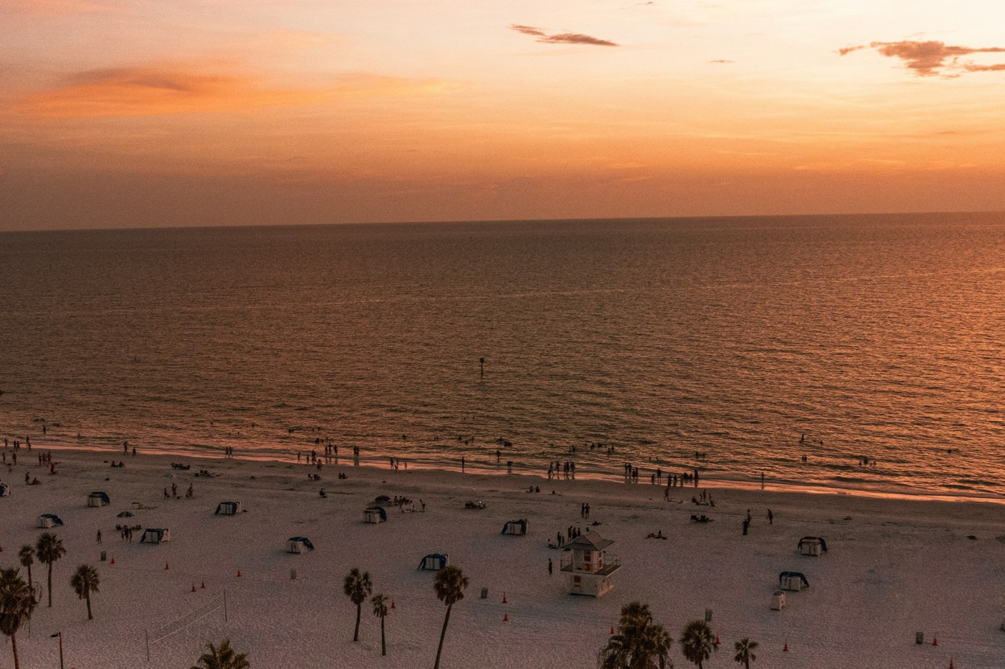 Miami Beach hosting dozens of beachgoers as the sun rises slightly out of view, bathing the beach in red-gold light