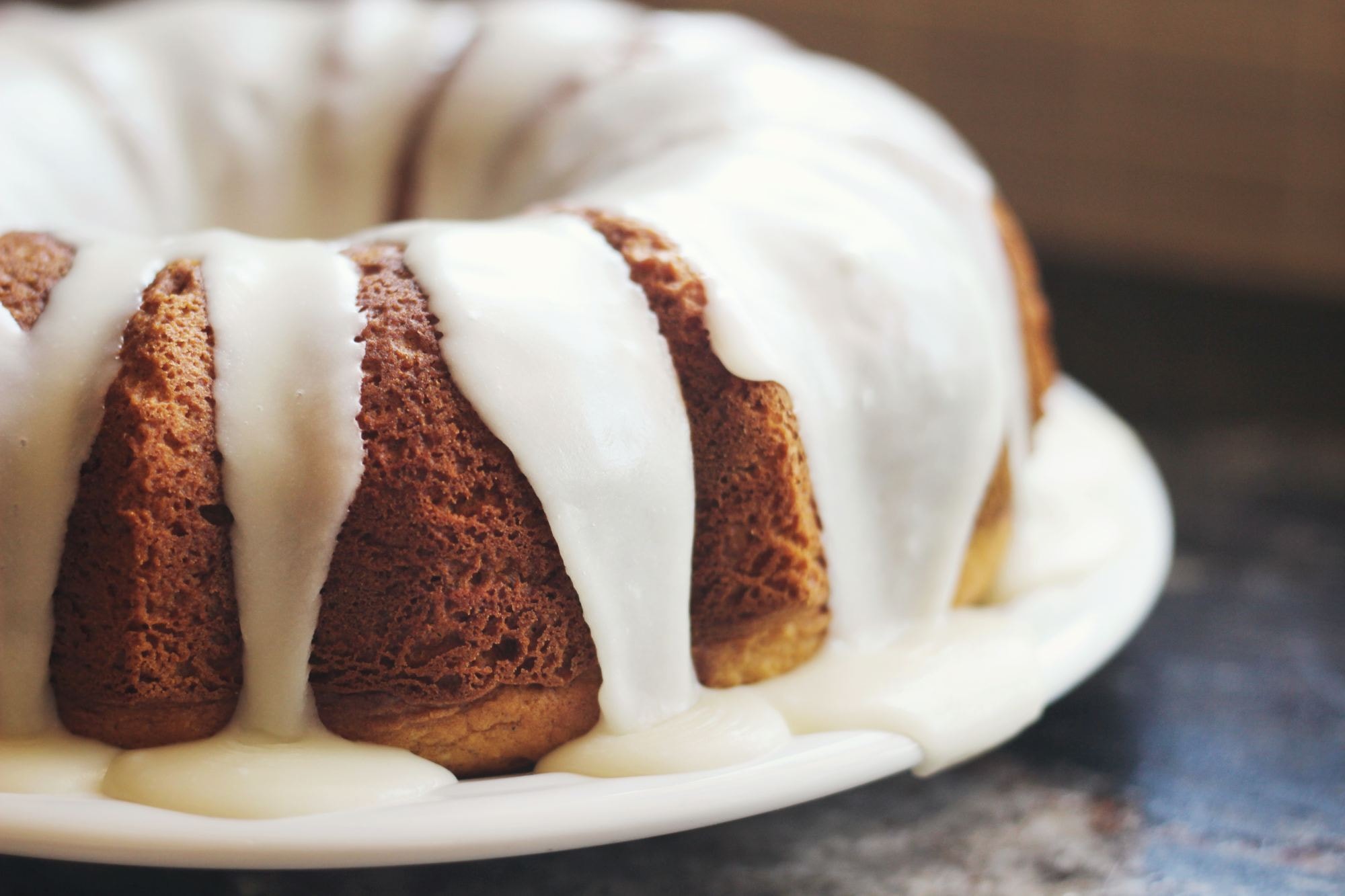 Delicious bundt cake with rich ivory colored icing dripping down the sides, sits on a plate on a countertop.