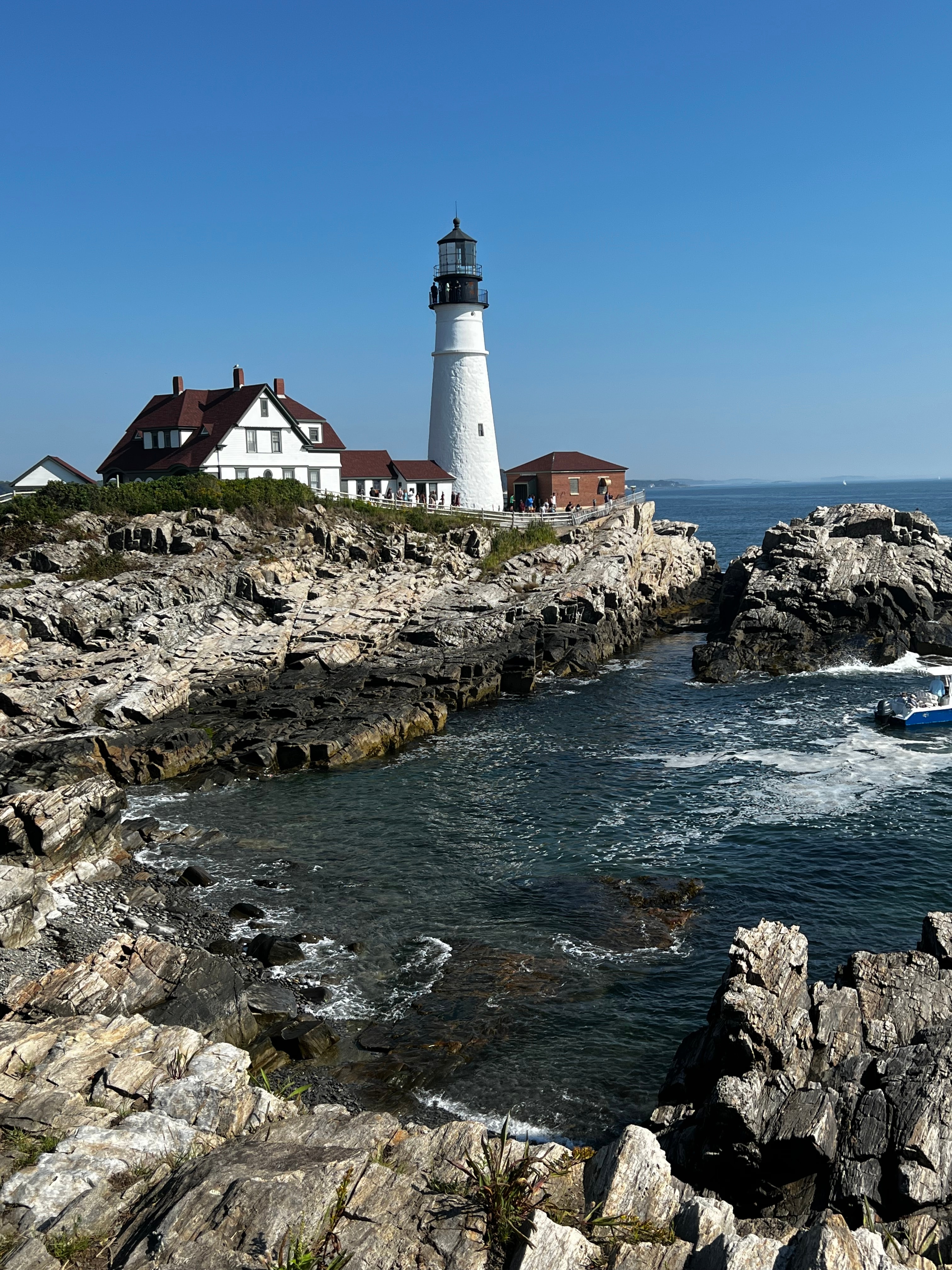 Picture of a lighthouse in Portland overlooking blue water and a rocky shoreline