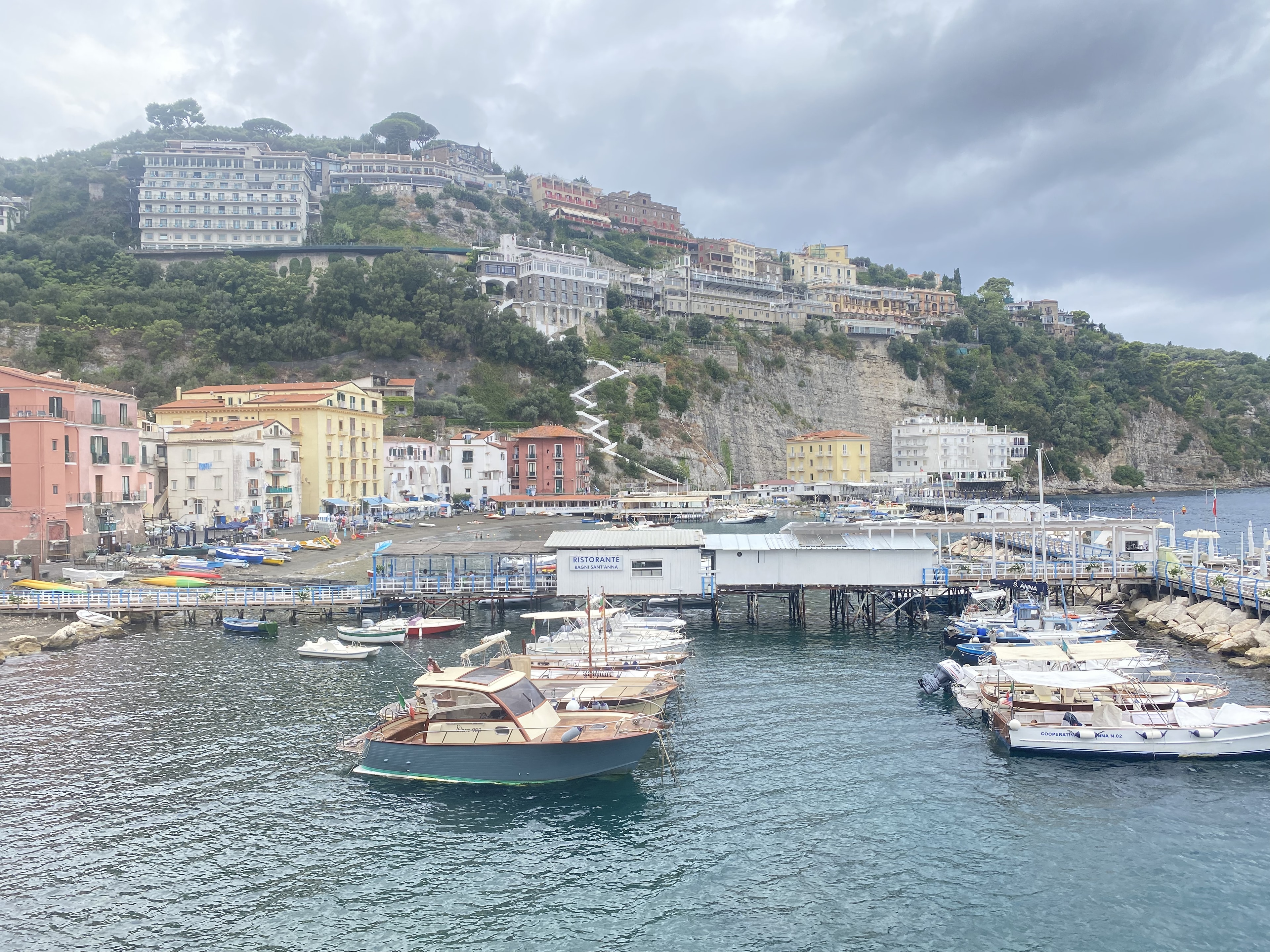 harbor with boats and a beautiful view of a seaside town built on a mountain. 