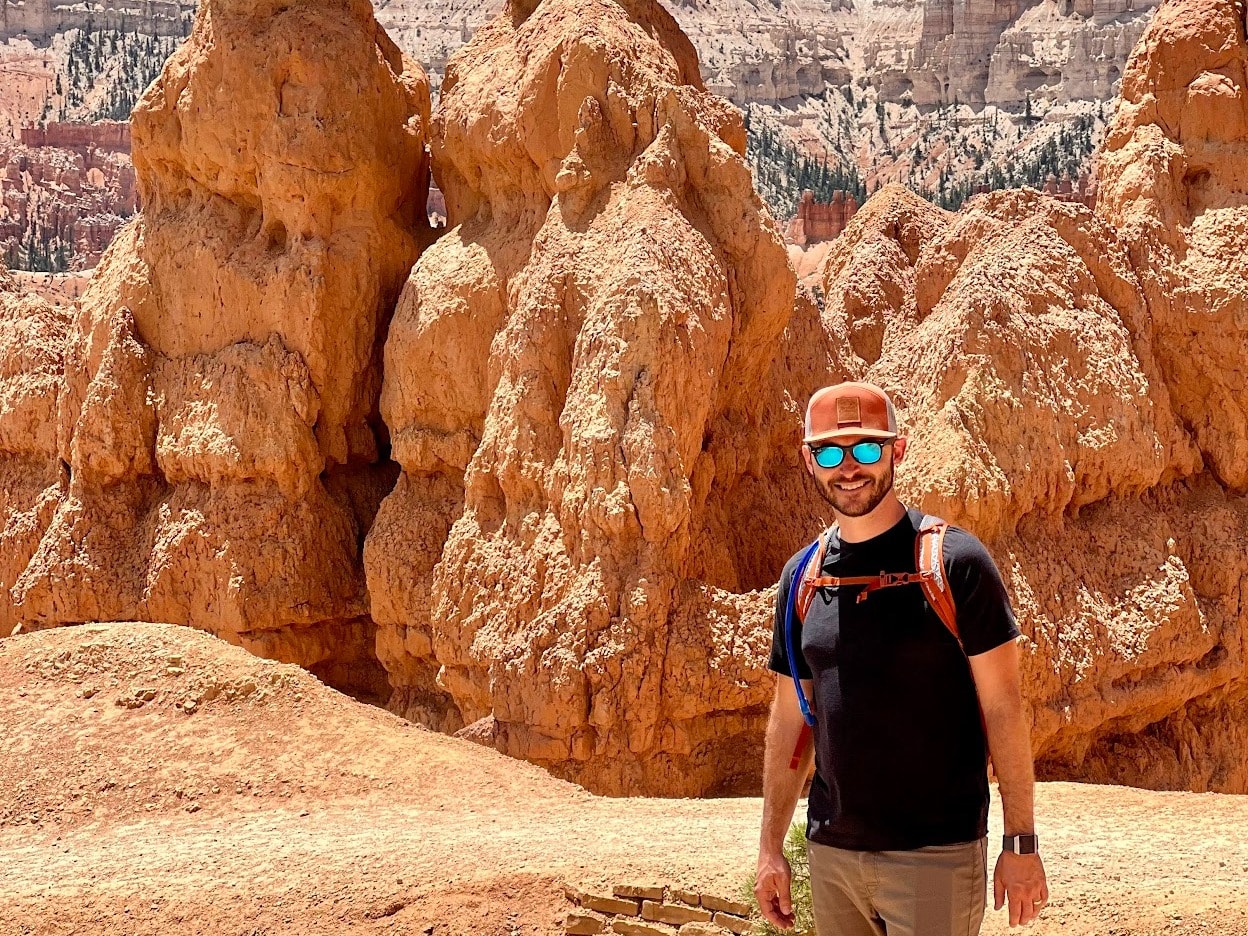 A man in black shirt standing in front of rock formations. 