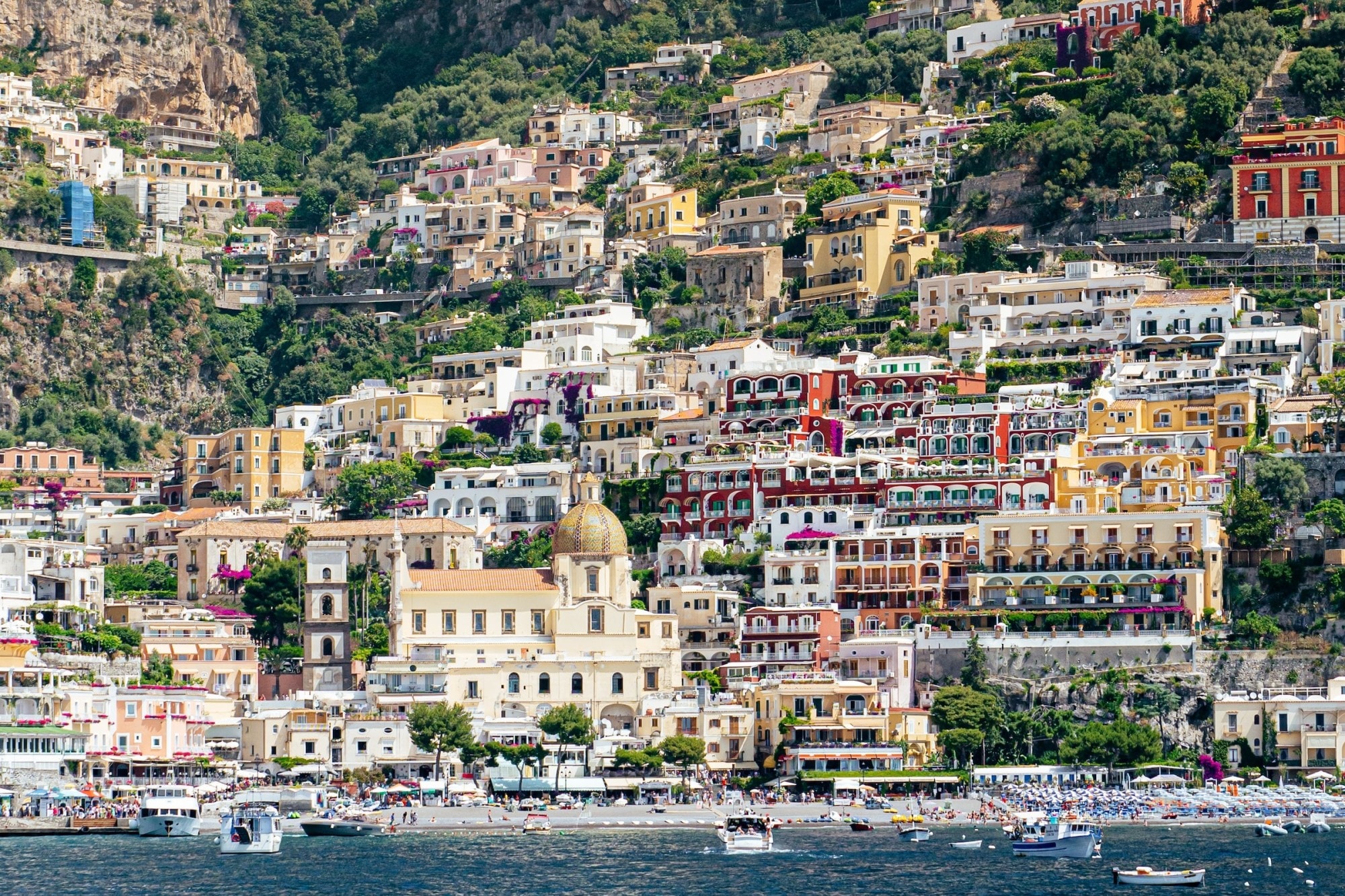 Cliff-bound homes and buildings stand above a dark-water shore filled with small watercraft