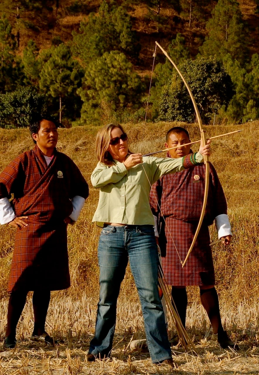 Travel advisor Allison shooting a bow and arrow surrounded by greenery with two men in brown robes watching on